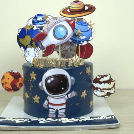 Space-themed cake with planets, rocket, and astronaut figurine on a dark blue background by Cakecroft.