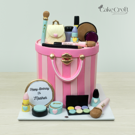 Makeup-themed handbag cake with edible cosmetics, including lipstick, eyeshadow, and brushes by Cakecroft