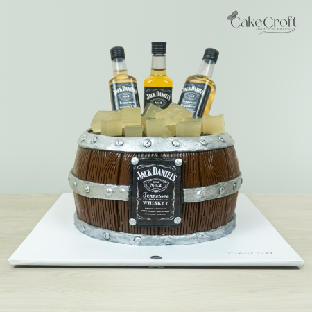 Jack Daniels-themed whiskey barrel cake with wooden barrel design, edible ice cubes, and miniature Jack Daniels bottles by Cakecroft.