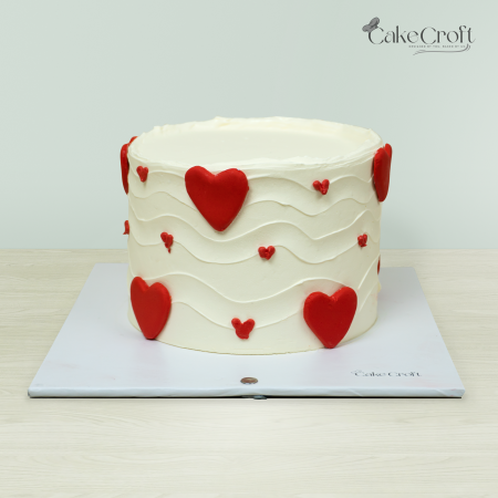 Heart-themed cake with white buttercream frosting and red heart decorations by Cakecroft