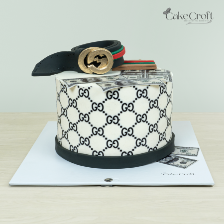 Gucci-themed cake with signature GG pattern, a golden belt buckle, and dollar bill decorations by Cakecroft.