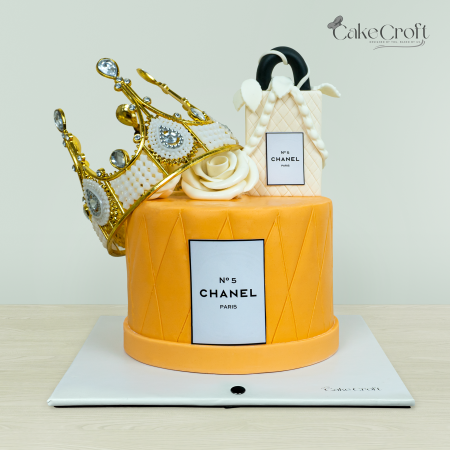 Chanel-inspired luxury cake with a golden crown, designer handbag, and floral accents by Cakecroft