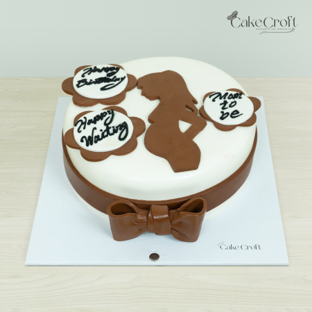 Mom-to-Be-themed cake with a silhouette of an expectant mother, brown bow, and plaques with messages by Cakecroft.