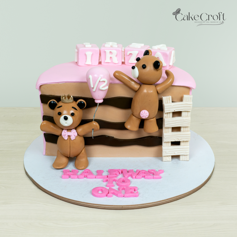 Halfway to One teddy bear-themed cake with two teddy bears, pink and brown accents, and a '1/2' balloon topper by Cakecroft.