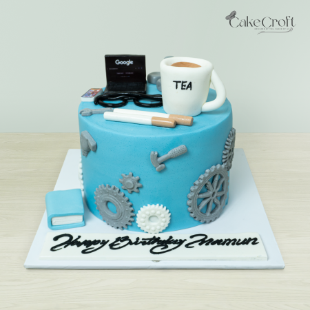 Blue tech-themed cake with fondant decorations of gears, tools, a laptop, and a cup labeled 'TEA,' perfect for engineers or tech lovers.