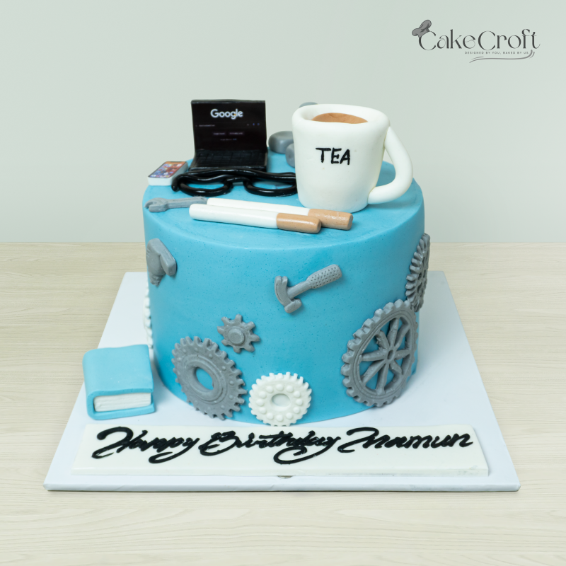 Blue tech-themed cake with fondant decorations of gears, tools, a laptop, and a cup labeled 'TEA,' perfect for engineers or tech lovers.