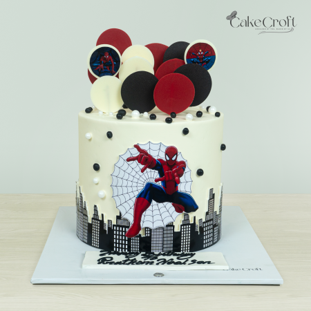 Spider-Man-themed cake with city skyline design, red, black, and white edible decorations, and a Spider-Man cutout in action