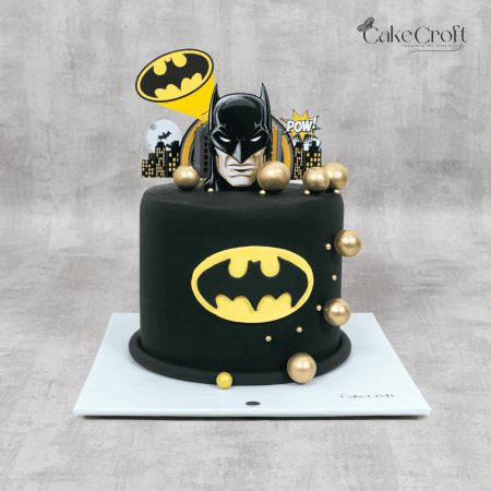 A black fondant Batman-themed cake featuring the iconic yellow logo, golden decorative spheres, and Gotham-inspired toppers.