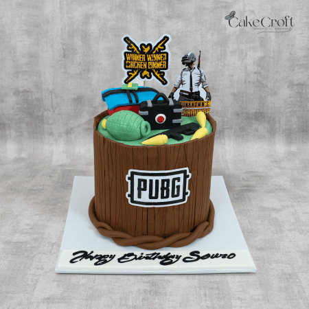 A PUBG-themed cake designed as a wooden barrel, featuring edible props like loot crates, grenades, and a 'Winner Winner Chicken Dinner' topper.