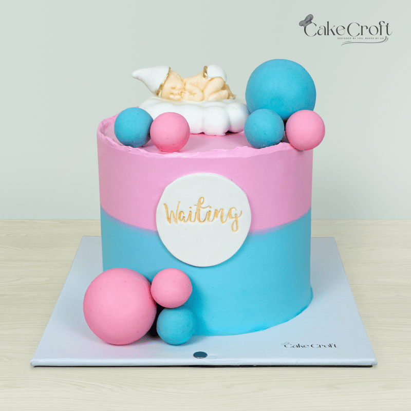 Pastel pink and blue gender reveal cake with a sleeping baby topper, decorative fondant spheres