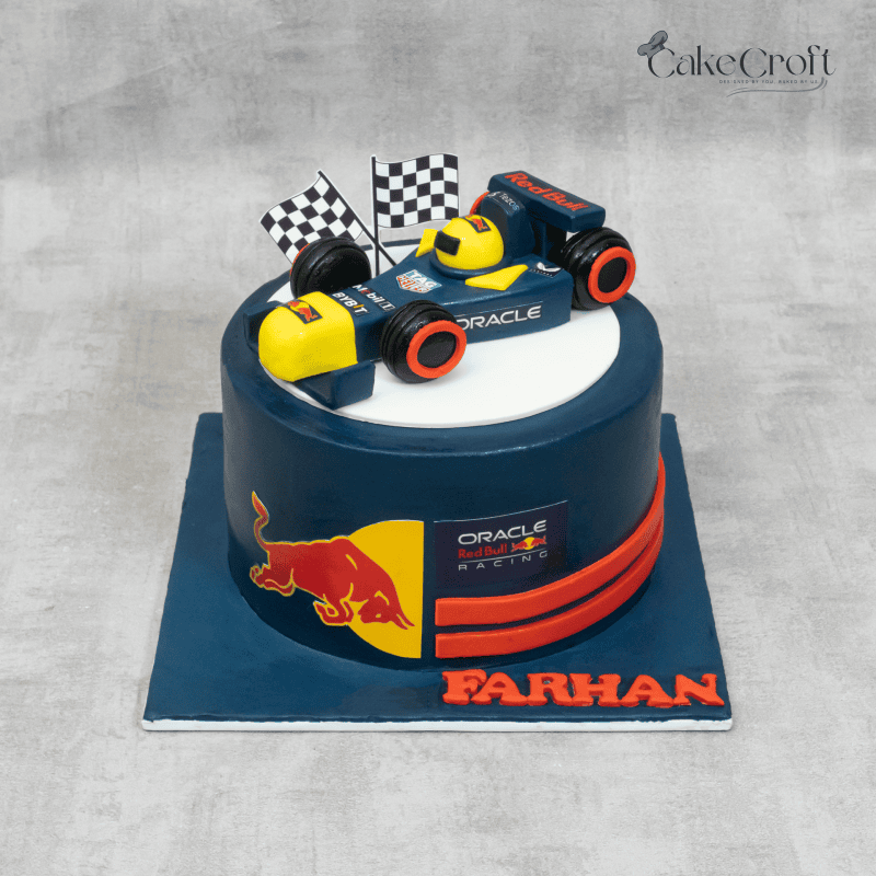 A Formula 1-themed cake with a Red Bull racing car, checkered flags, and Red Bull logos on a sleek blue fondant base.