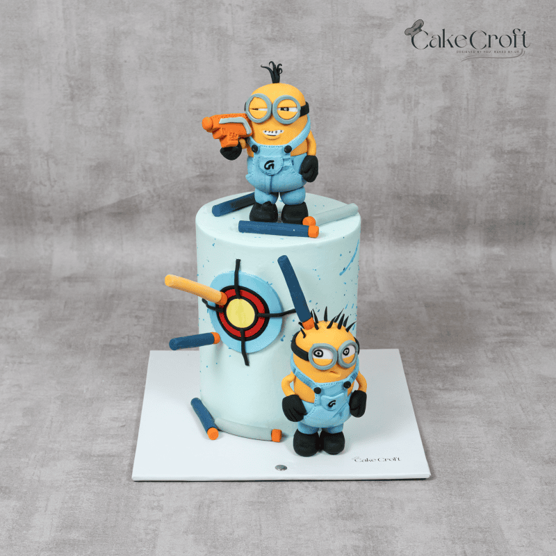 A Minion-themed cake with fondant Minion characters, a colorful target design, and Nerf-inspired darts, perfect for kids' celebrations