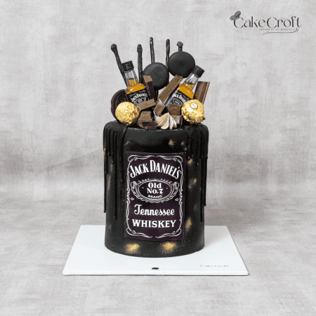 A black fondant Jack Daniel’s-themed cake with gold accents, dripping ganache, mini whiskey bottles, and Ferrero Rocher chocolates.