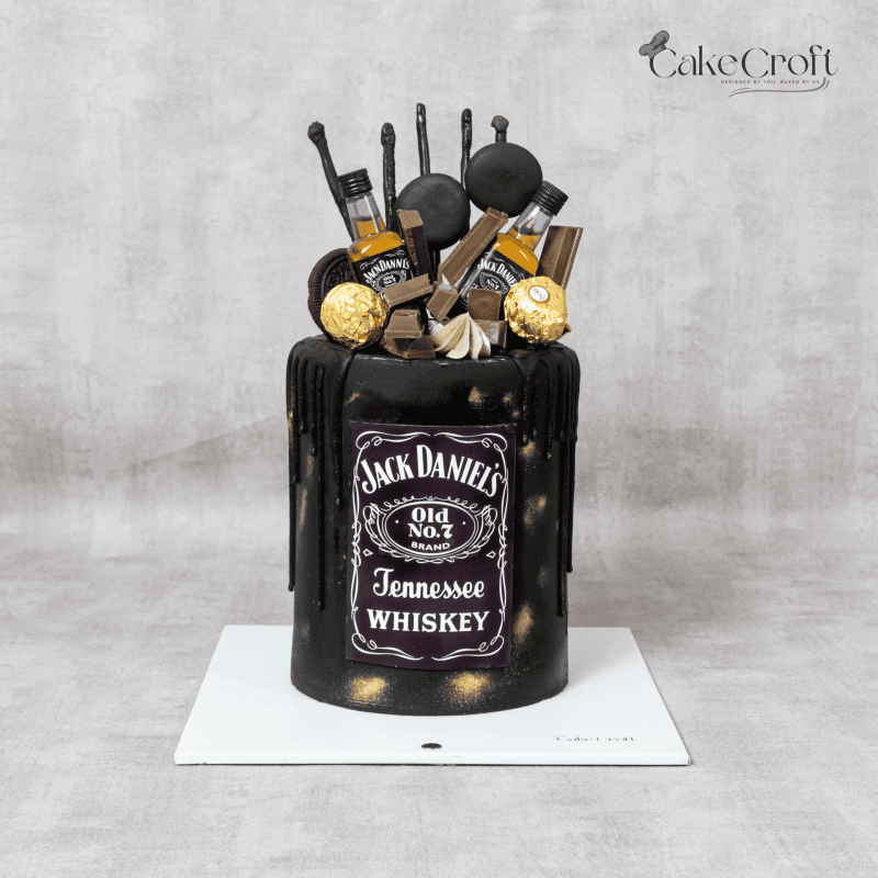 A black fondant Jack Daniel’s-themed cake with gold accents, dripping ganache, mini whiskey bottles, and Ferrero Rocher chocolates.