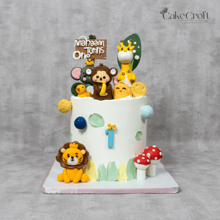 A jungle-themed birthday cake with fondant animals, including a lion, giraffe, and monkey, decorated with mushrooms and playful accents.