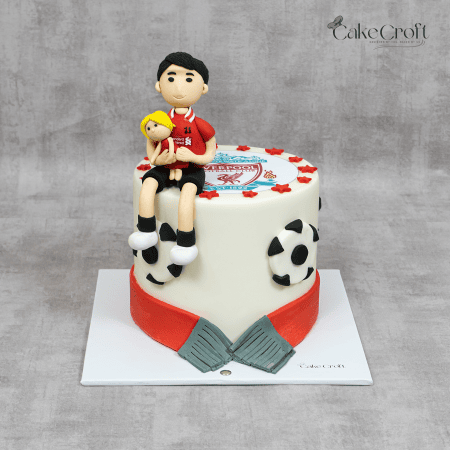 A Liverpool FC-themed cake with a fondant player, team logo, football accents, and a red scarf detail.