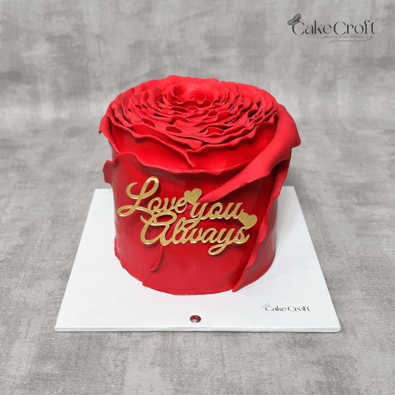 A romantic rose-shaped red fondant cake with "Love You Always" in golden accents.