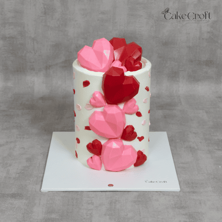 A modern white cake decorated with 3D pink and red geometric hearts, perfect for romantic celebrations like Valentine’s or anniversaries.