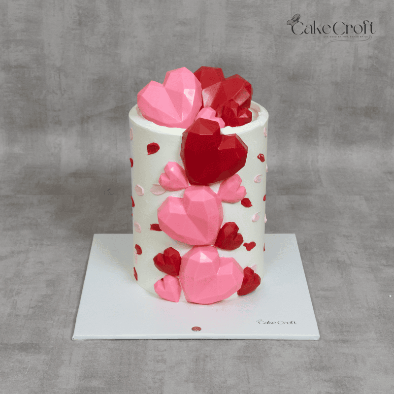 A modern white cake decorated with 3D pink and red geometric hearts, perfect for romantic celebrations like Valentine’s or anniversaries.