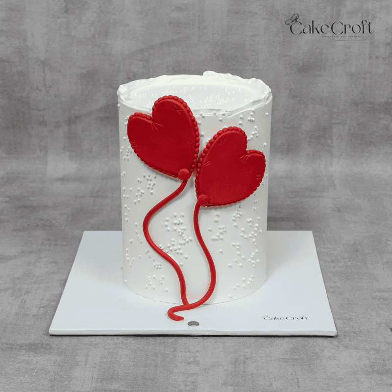 A minimalist white textured cake with vibrant red heart-shaped fondant balloons, perfect for romantic celebrations.