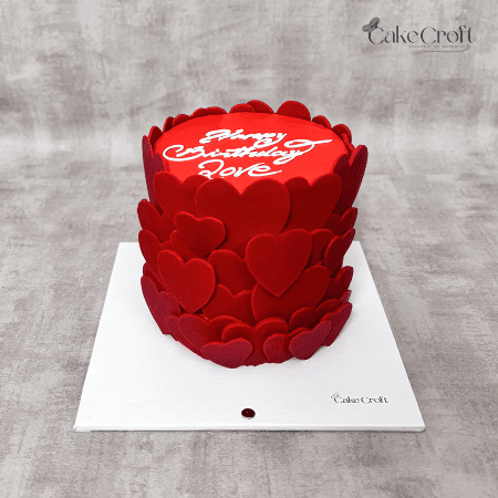 A vibrant red cake adorned with cascading fondant hearts and a smooth finish, perfect for romantic celebrations like Valentine’s or anniversaries.