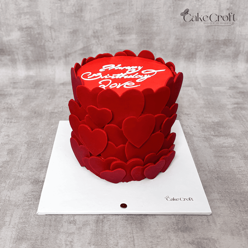 A vibrant red cake adorned with cascading fondant hearts and a smooth finish, perfect for romantic celebrations like Valentine’s or anniversaries.