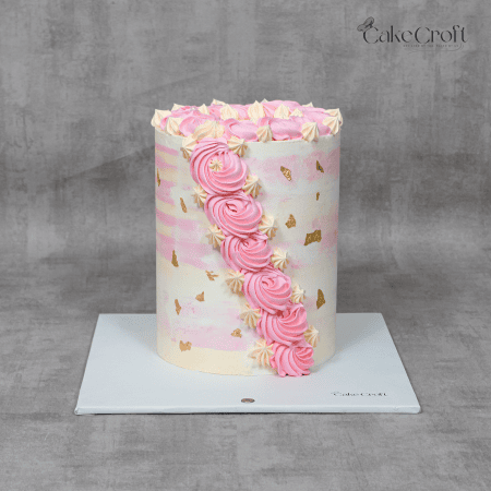 A beautifully crafted pastel pink and white cake adorned with a cascading swirl of pink buttercream roses and delicate golden accents.