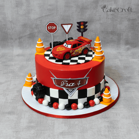 A bold red racing cake with a checkered finish line, road signs, and a Lightning McQueen topper