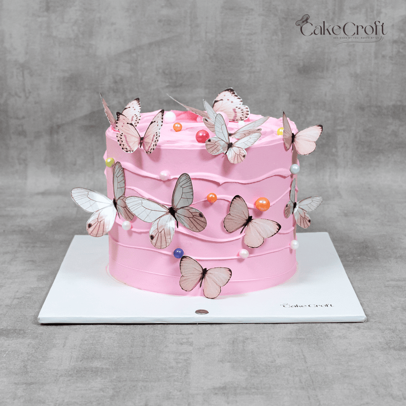 A pink butterfly cake with delicate edible butterflies, pastel pearl accents, and soft buttercream swirls, perfect for birthdays, baby showers, or special celebrations.