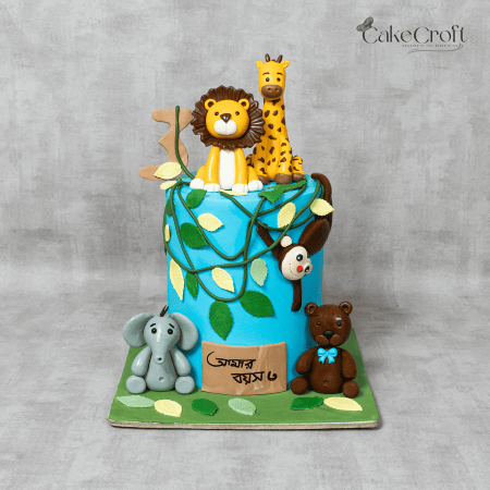 A vibrant jungle-themed cake featuring fondant animal toppers including a lion, giraffe, elephant, monkey, and bear, surrounded by lush green leaves and vines.