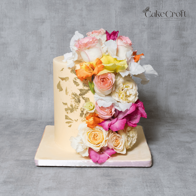 A luxurious floral cascade cake adorned with fresh roses, orchids, and gold leaf detailing. Perfect for weddings, anniversaries, and elegant celebrations.