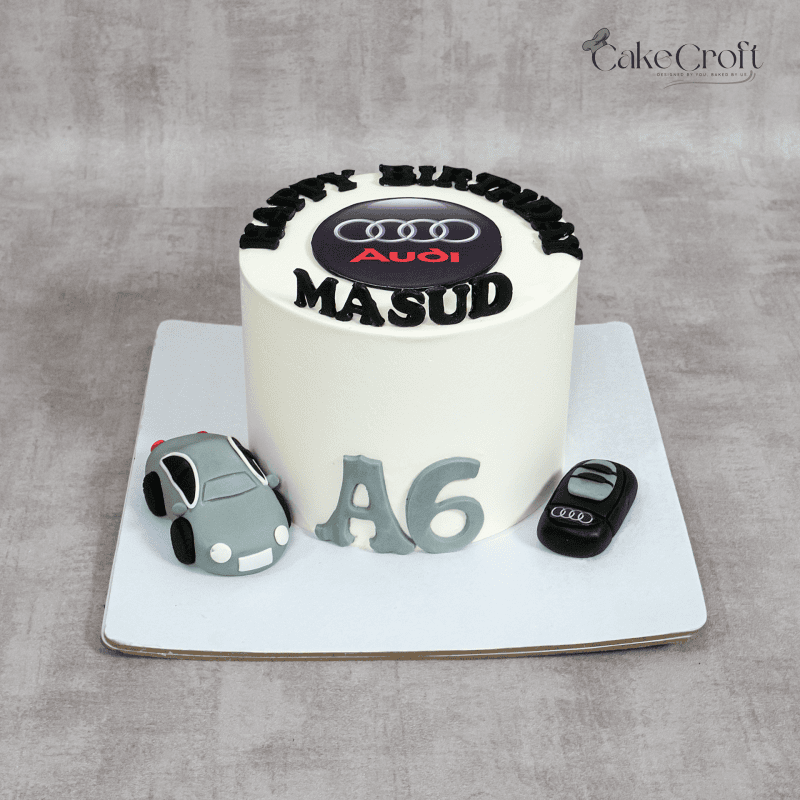 A luxury Audi-themed birthday cake featuring a sleek white fondant base, edible Audi logo topper, a fondant car, car key, and "A6" lettering for a premium automotive-inspired celebration.