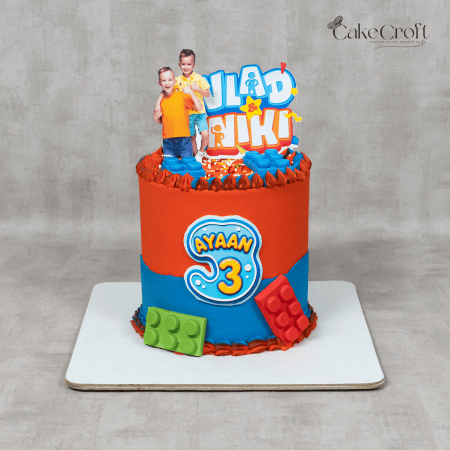 A colorful Vlad & Niki theme birthday cake with a blue and orange design, featuring LEGO-inspired decorations and a custom name topper.