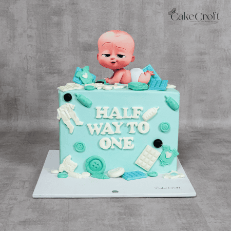 A baby blue half-birthday cake featuring a cute Boss Baby topper, fondant baby essentials, and the text "Half Way to One."