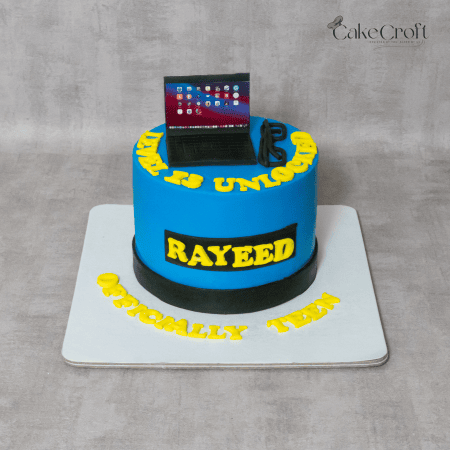 A blue and black birthday cake with a mini edible laptop, yellow text, and a "Level 13 Unlocked" gaming-inspired theme. The cake features the name "Rayeed" and "Officially Teen" written in bold yellow fondant letters.