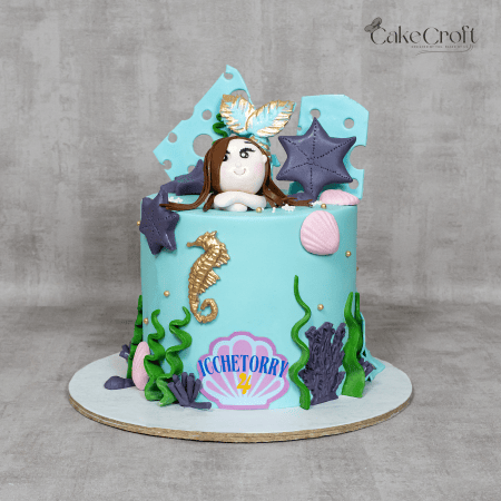 A beautifully crafted mermaid-themed birthday cake featuring an adorable fondant mermaid, seashells, starfish, seaweed, and gold accents.