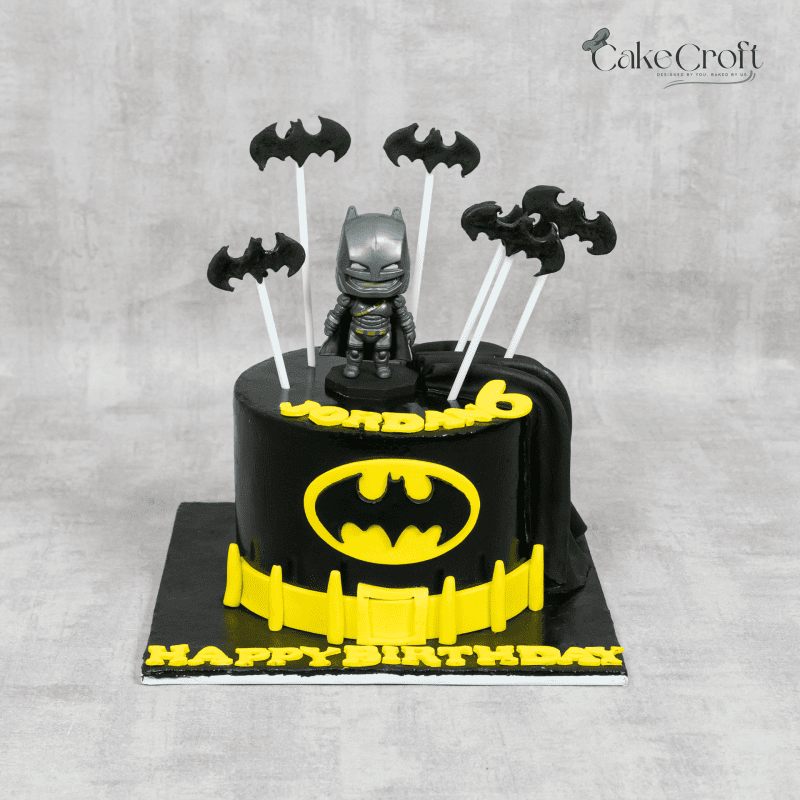 A black and yellow Batman-themed birthday cake featuring a Batman figure, bat symbols, and a fondant utility belt.