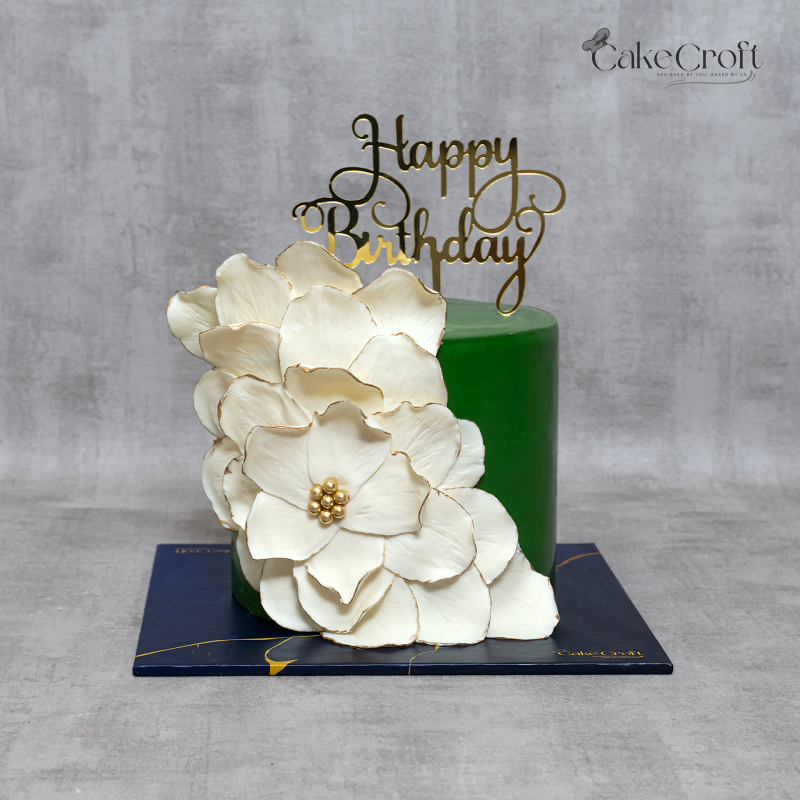 Elegant green birthday cake with large white flower petals and golden birthday topper