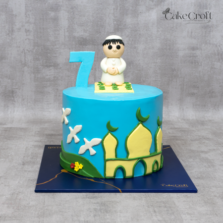 Sky blue birthday cake featuring a mosque design and a fondant boy in prayer with number 7 topper