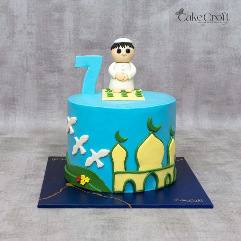 Sky blue birthday cake featuring a mosque design and a fondant boy in prayer with number 7 topper