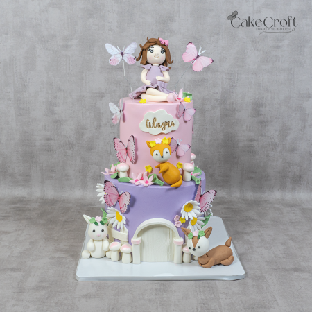 Two-tier pastel birthday cake with butterflies, woodland animals, and a fondant girl topper