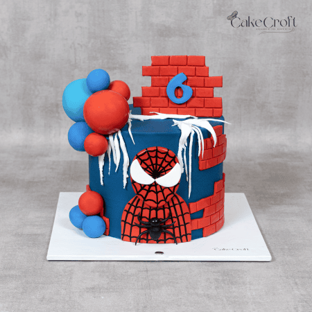 Spiderman birthday cake decorated with red brick pattern, blue fondant, spiderweb icing, and balloon toppers.