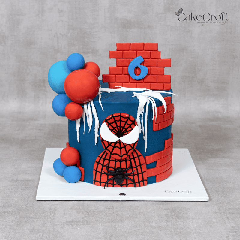 Spiderman birthday cake decorated with red brick pattern, blue fondant, spiderweb icing, and balloon toppers.