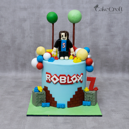 Roblox-themed birthday cake with fondant character topper, colorful balloon decorations, and LEGO-style bricks for a 7th birthday celebration.