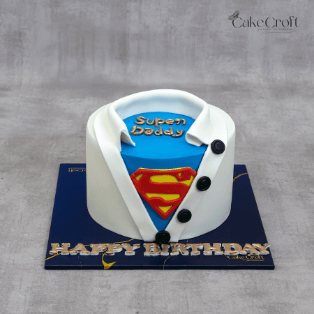 A superhero-themed cake designed like a shirt opening to reveal a blue undershirt with a Superman logo and the words "Super Daddy" on top.