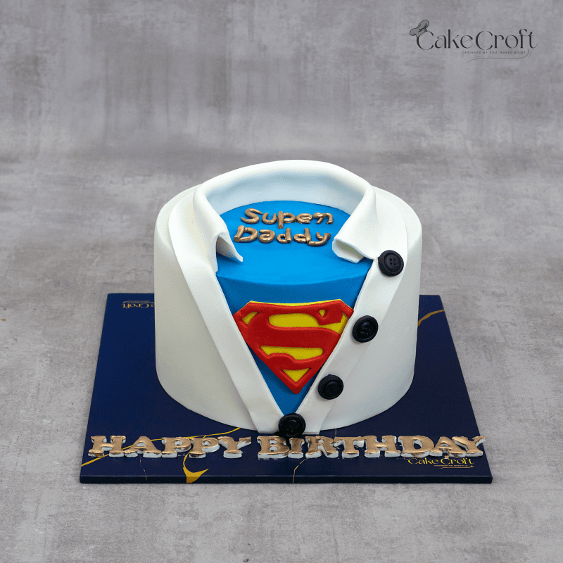 A superhero-themed cake designed like a shirt opening to reveal a blue undershirt with a Superman logo and the words "Super Daddy" on top.
