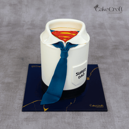 A tall fondant cake designed like a shirt and tie, revealing a Superman logo underneath, with "Super Dad" written on the shirt pocket.