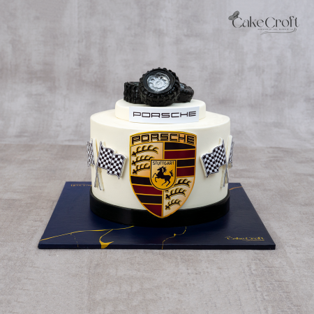 Porsche-themed fondant cake with ivory base, Porsche crest, racing flags, and black tire topper by CakeCroft Dhaka.