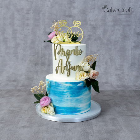 Two-tier blue and white wedding cake with gold lettering, floral decorations, and “Mr & Mrs” topper by CakeCroft Dhaka.