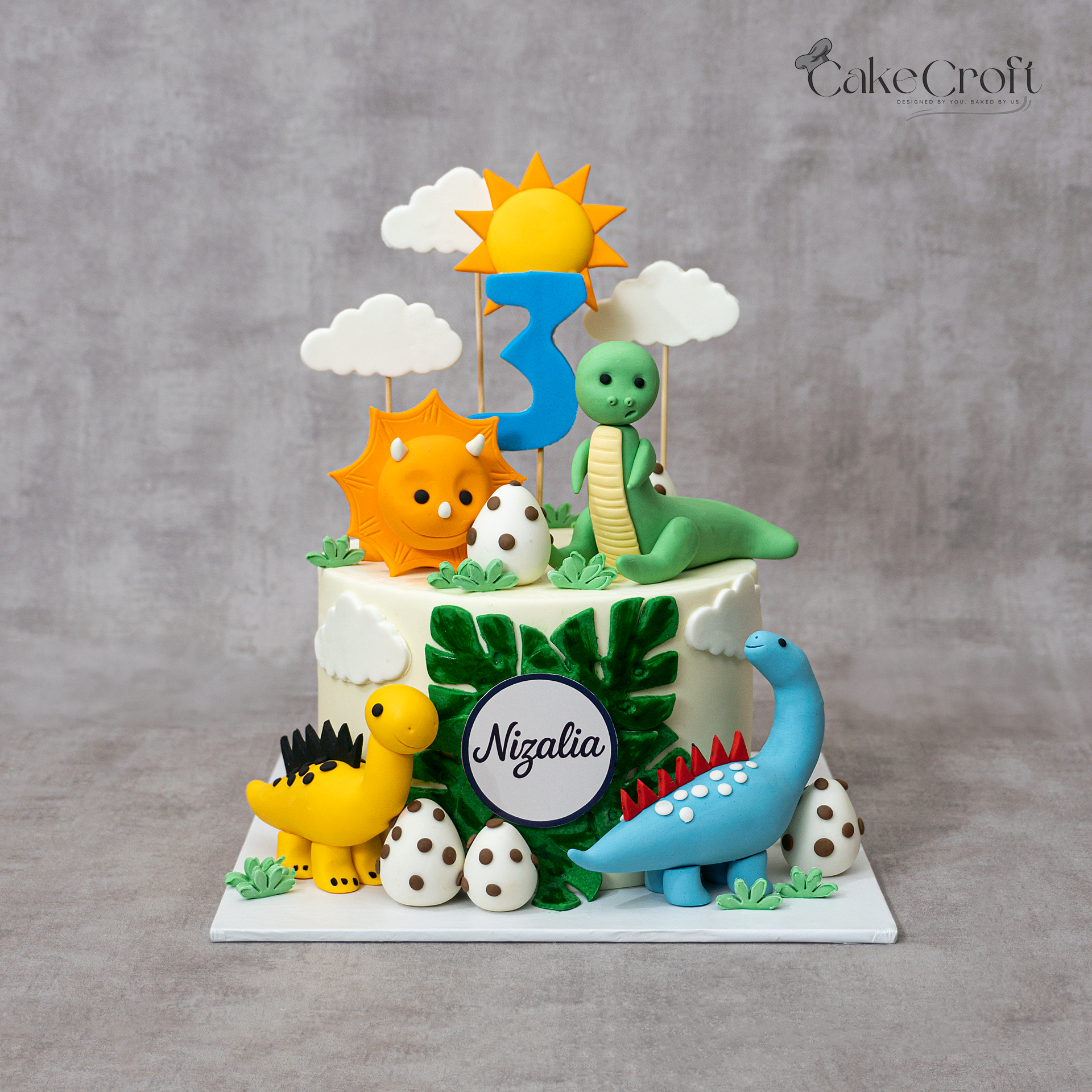 Dinosaur themed fondant cake with colorful dinosaurs, dino eggs, sun, clouds, and number 3 topper by CakeCroft Dhaka.